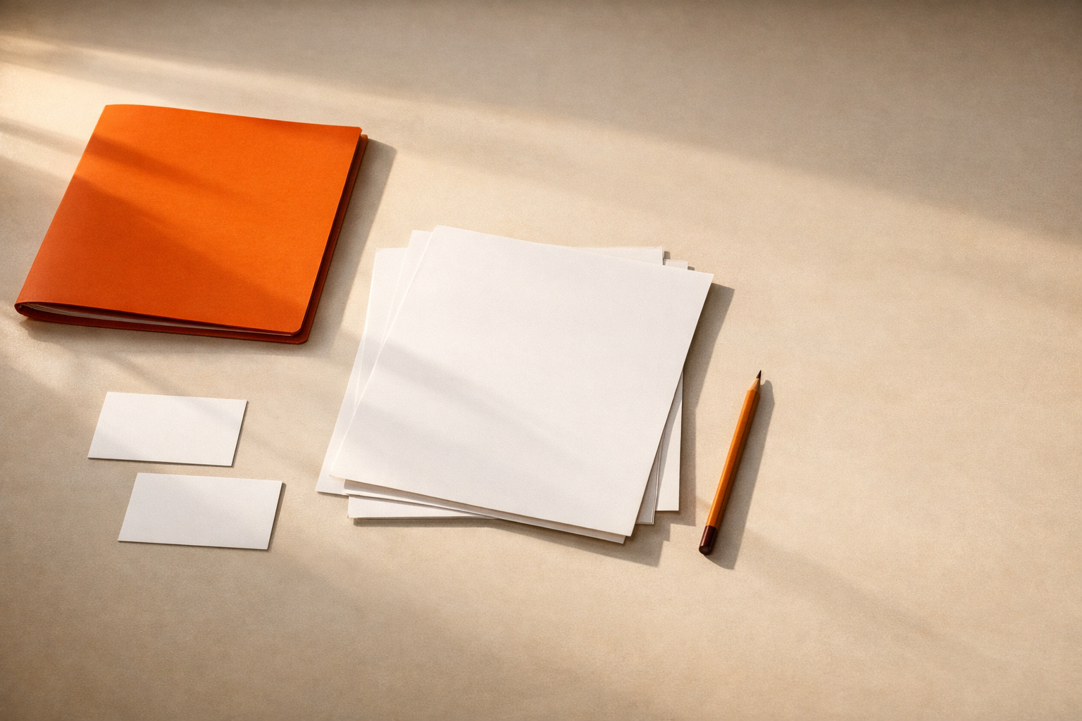 Minimal editorial still life: blank sheets, a closed orange folder, and a pencil in warm light on a clean neutral table, evoking active personal planning. No visible text or people.